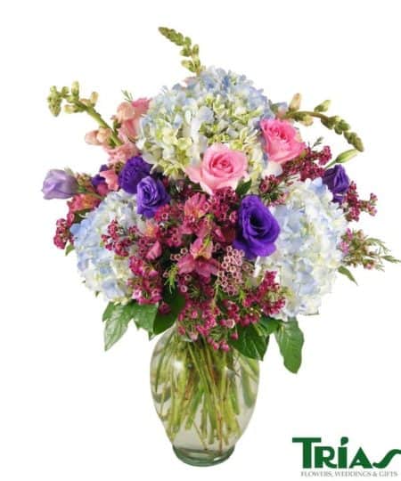 A magnificent arrangement of natures finest blue hydrangeas, pink roses, alstromerias, snapdragons, purple lisianthus and eucalyptus in a glass vase.